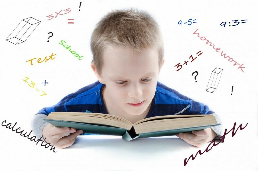 Young white child reading a book and surrounded by math problems and math related text. Fun math puzzles kids could provide him with more learning tools.