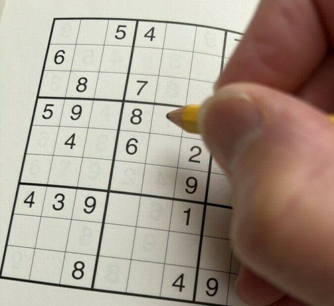 Picture of person using paper Sudoku puzzle for a comparison to wooden sudoku board game set