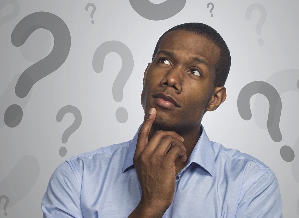 Black man surrounded by question marks and pondering how to solve easy cryptic crosswords