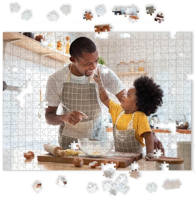 picture of black man and young child looking at each other and smiling as they cook in the kitchen. the picture is made into a jigsaw puzzle.