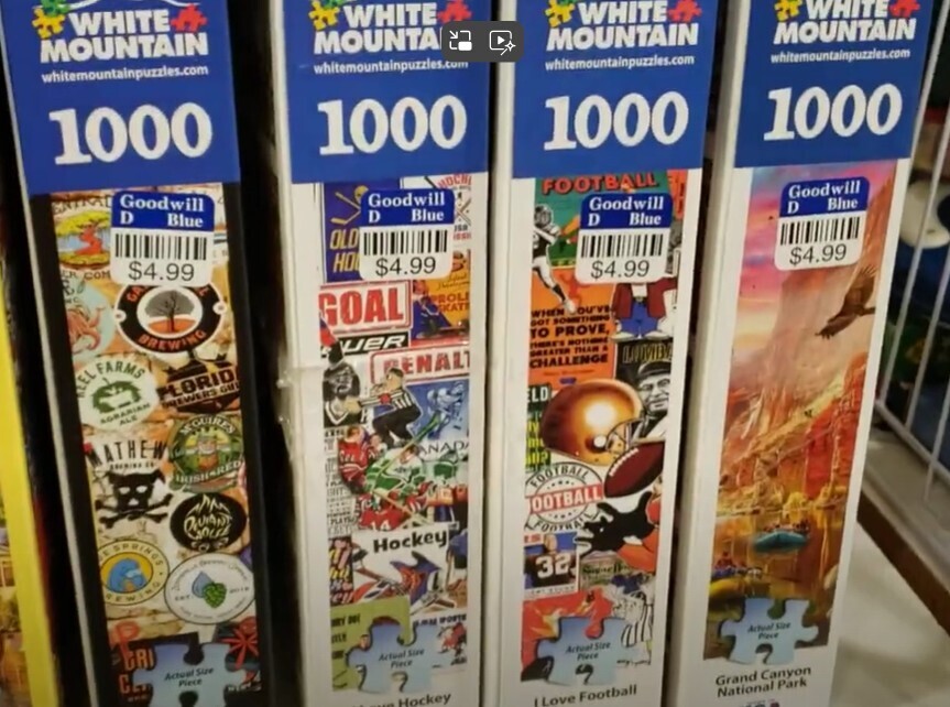 Four used jigsaw puzzles side by side on a Goodwill store shelf